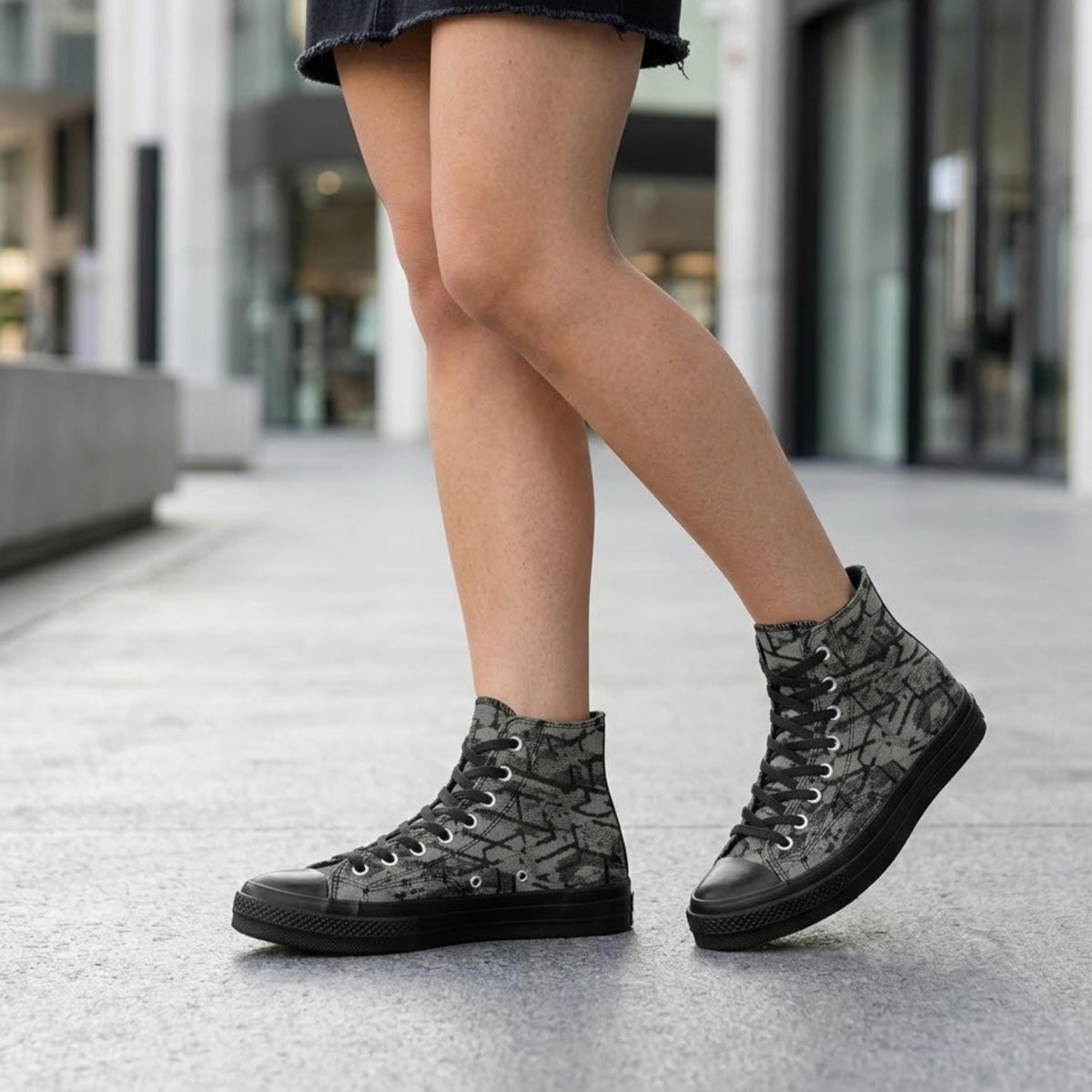 A person wearing black and gray patterned sneakers is standing on a sidewalk.