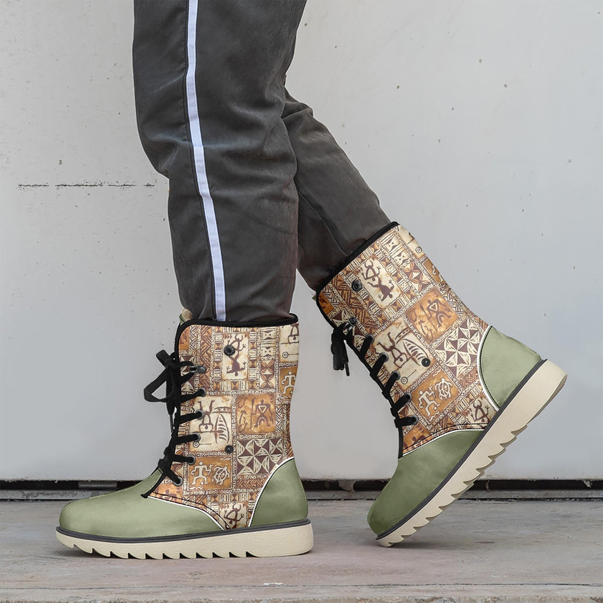 A person wearing a pair of patterned green and beige boots stands against a white wall.