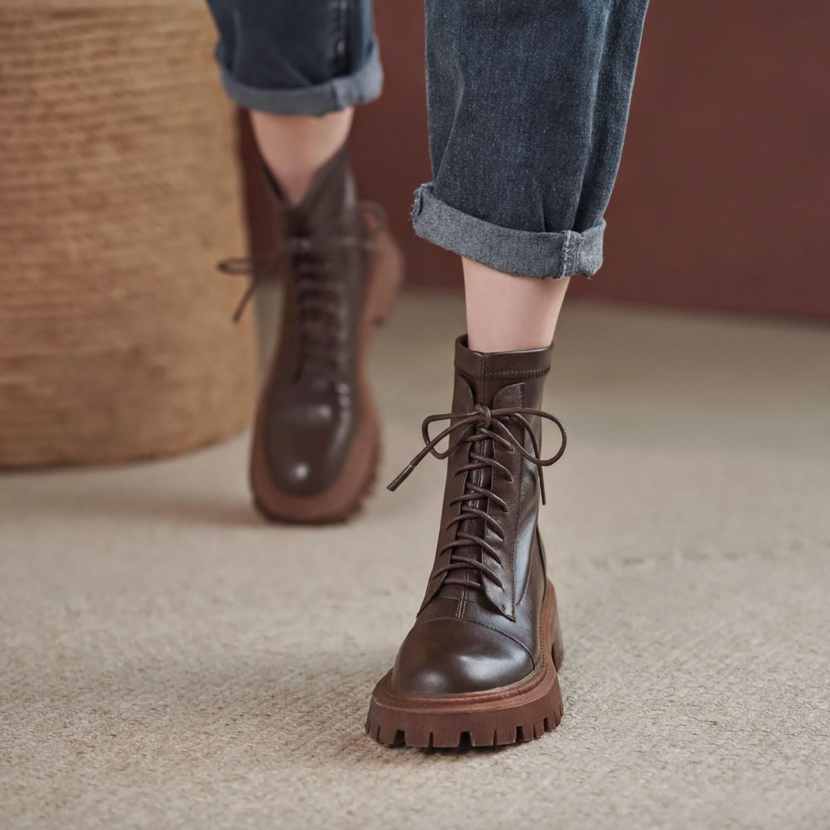 A close-up of a person's feet wearing brown leather boots with laces, standing on a carpeted floor.