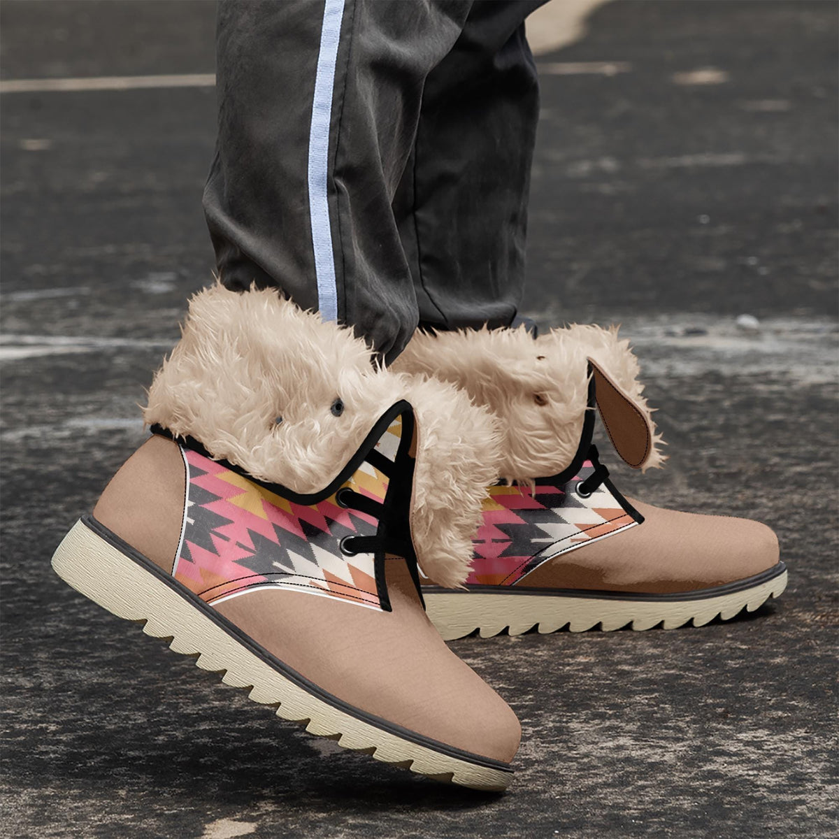 A pair of tan boots with a colorful patterned design, featuring fur trim and laces, are shown on a black surface.