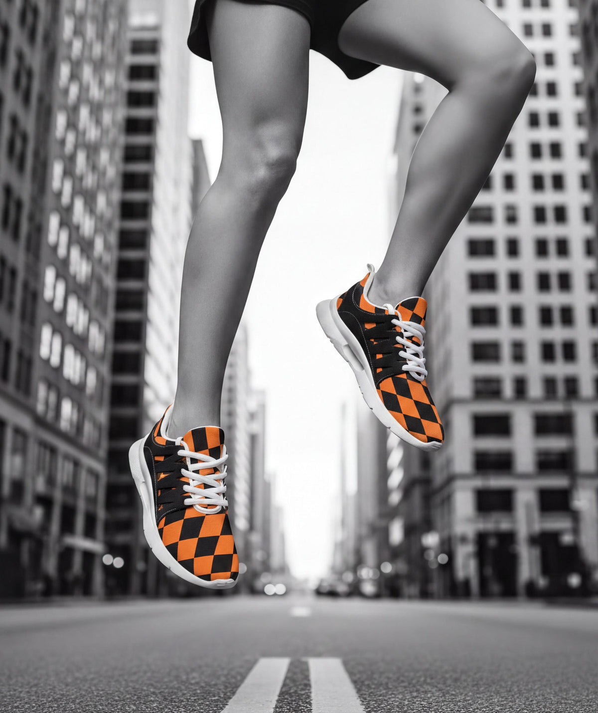 A person wearing orange and black checkered sneakers is captured mid-jump in a city street, with tall buildings in the background.