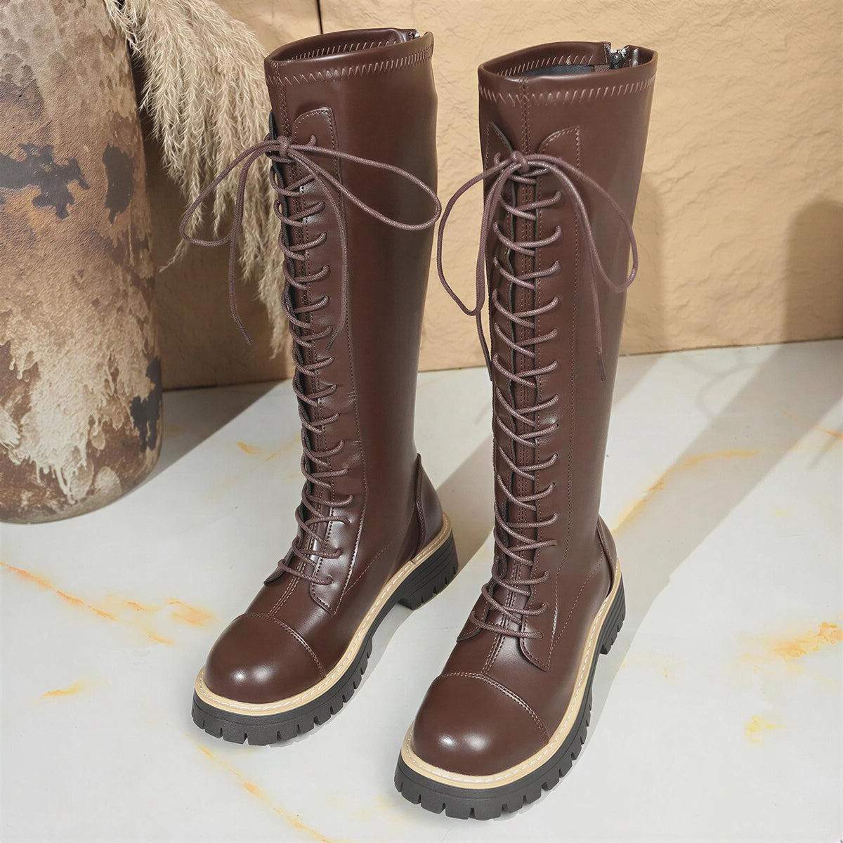 A pair of brown leather boots with laces and a thick sole, placed on a white surface.