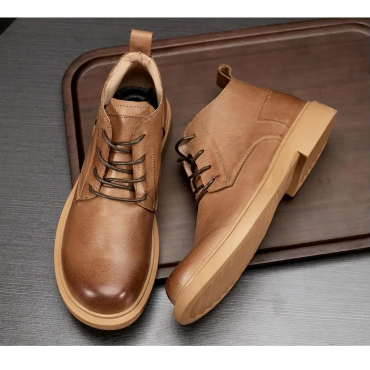A pair of brown leather boots with laces and a chunky sole, placed on a wooden surface.