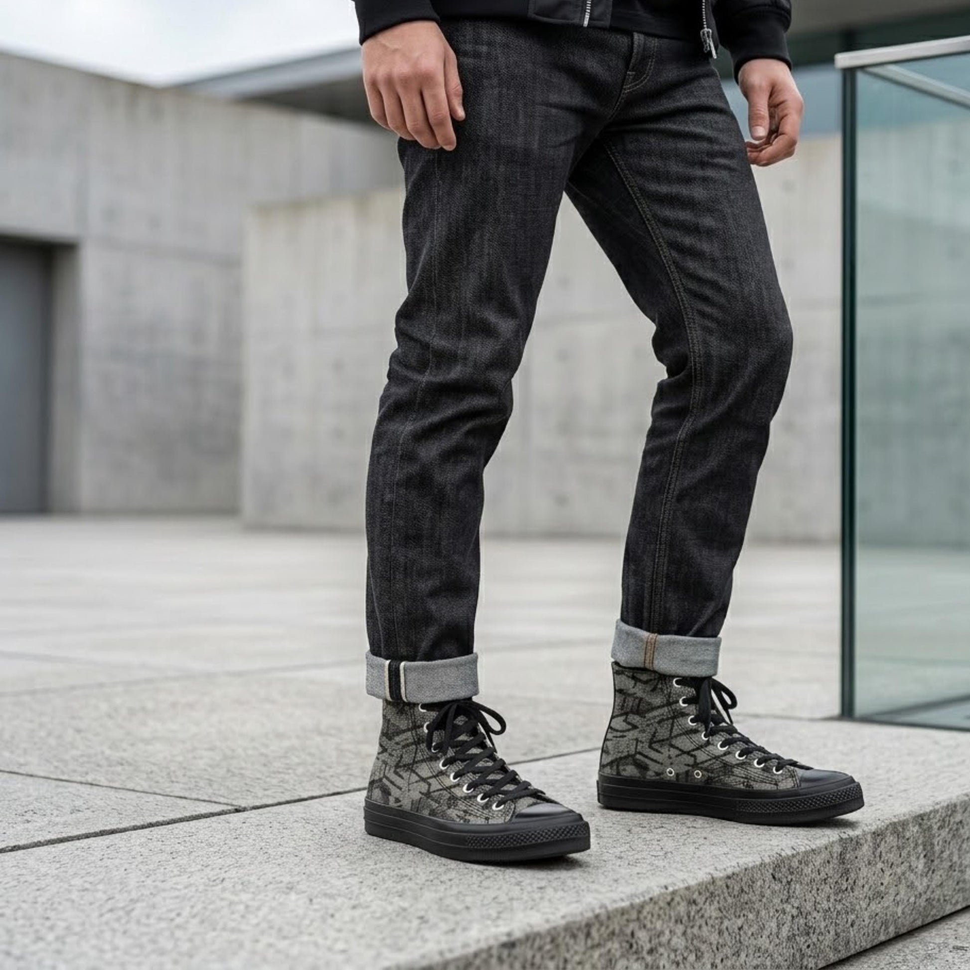 A person wearing black jeans and black and gray sneakers stands on a concrete ledge.
