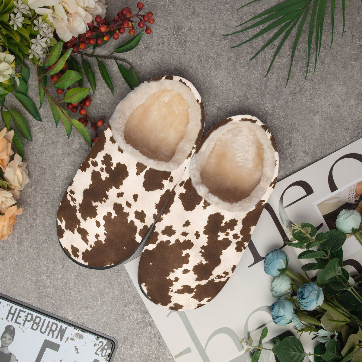 Vista cenital de un par de zapatillas de casa de vaca sobre una superficie gris con flores y una revista