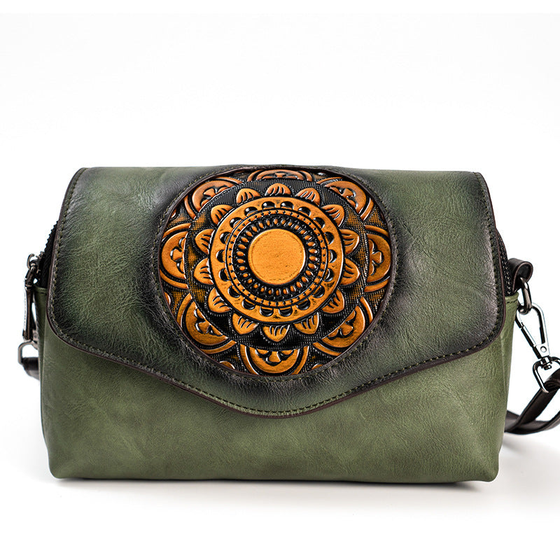 An olive green faux leather crossbody bag featuring a large, circular, hand-tooled floral mandala design in orange-brown on the front flap, set against a plain white background.