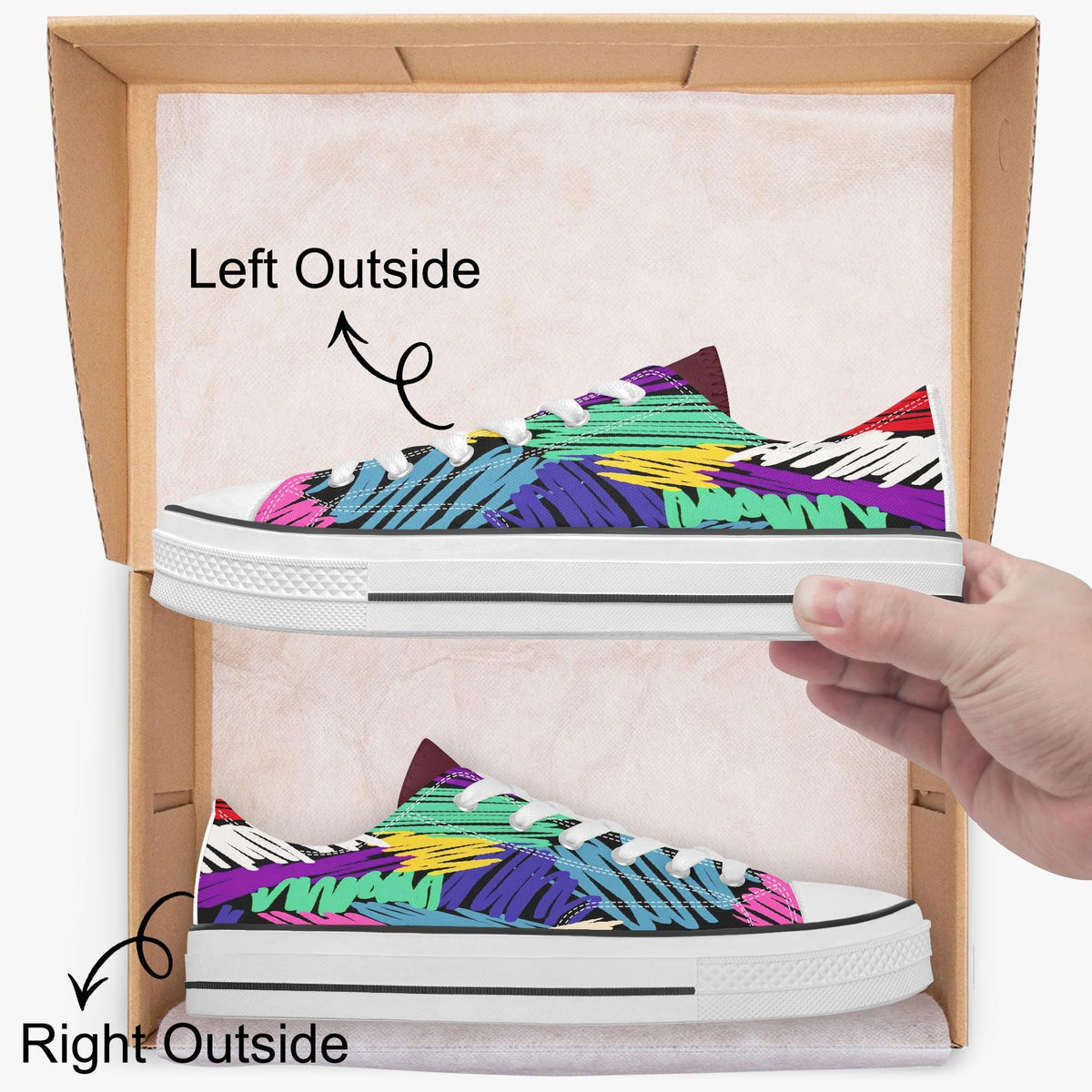 A hand is holding a pair of colorful, patterned sneakers inside a cardboard box, with the left shoe positioned outside the box and the right shoe inside.