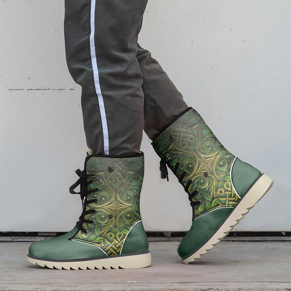 A person wearing green and gold patterned boots stands against a white wall.