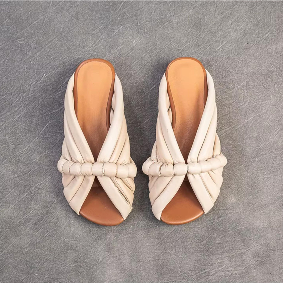 A pair of beige leather sandals with a unique, twisted design.