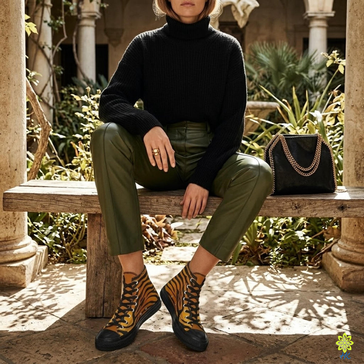 A person wearing a black sweater, green pants, and yellow and black tiger-striped boots is sitting on a wooden bench in a garden setting.