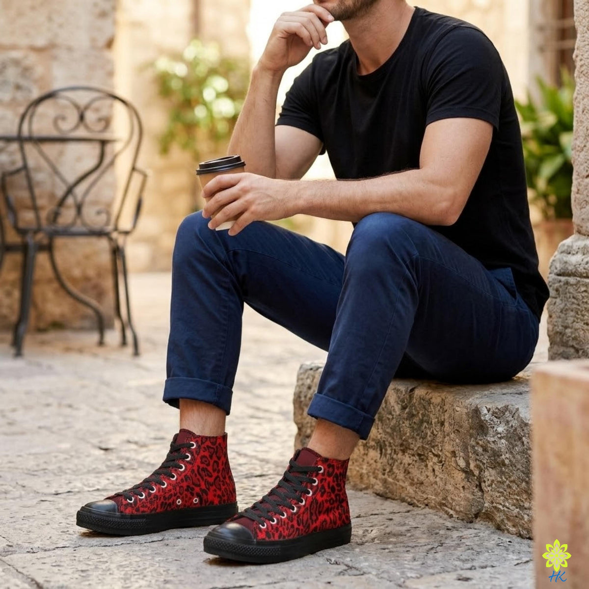 A man is sitting on a stone step, holding a coffee cup in his hand and wearing red and black sneakers.