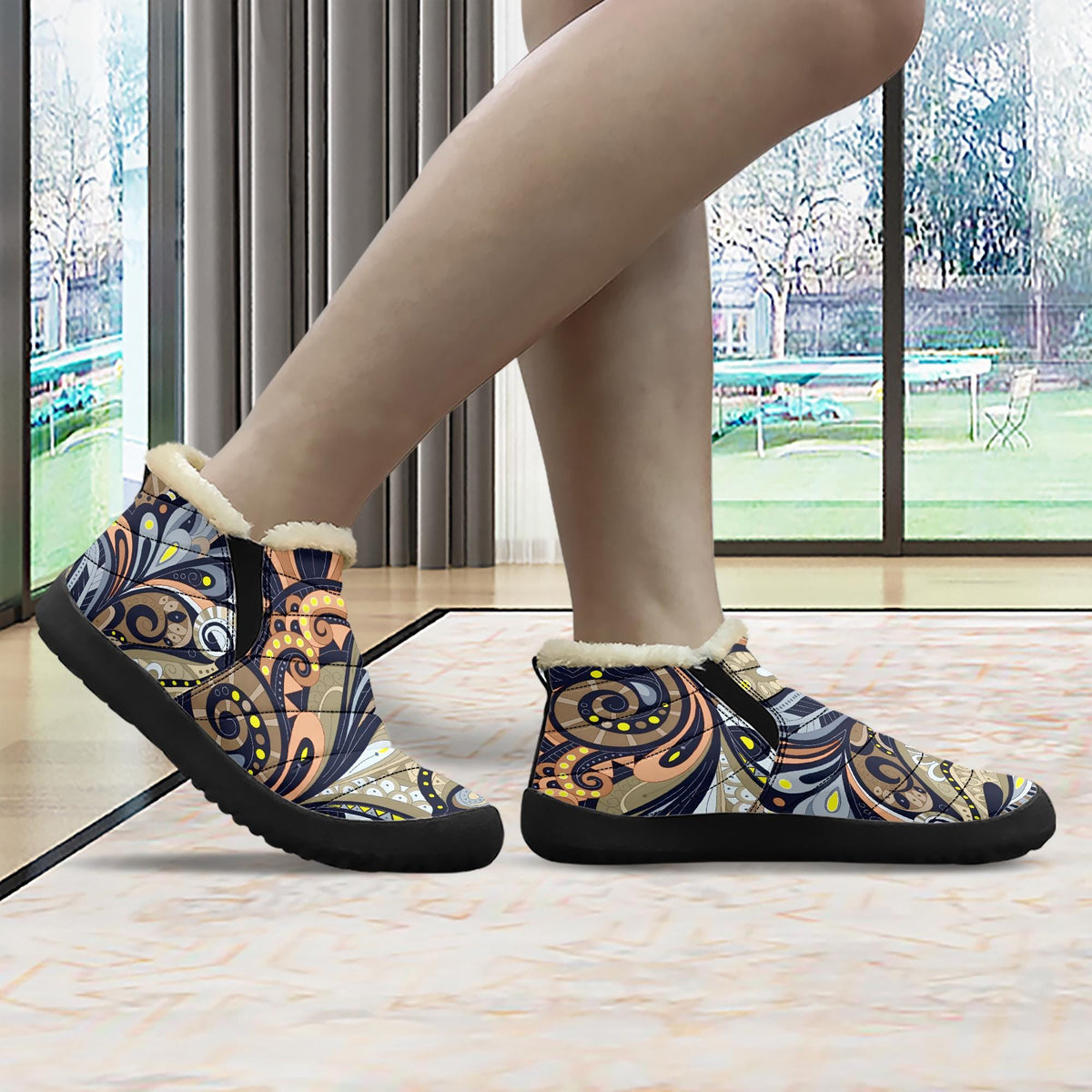 A person's feet wearing colorful patterned shoes, standing in front of a window with a view of a garden outside.