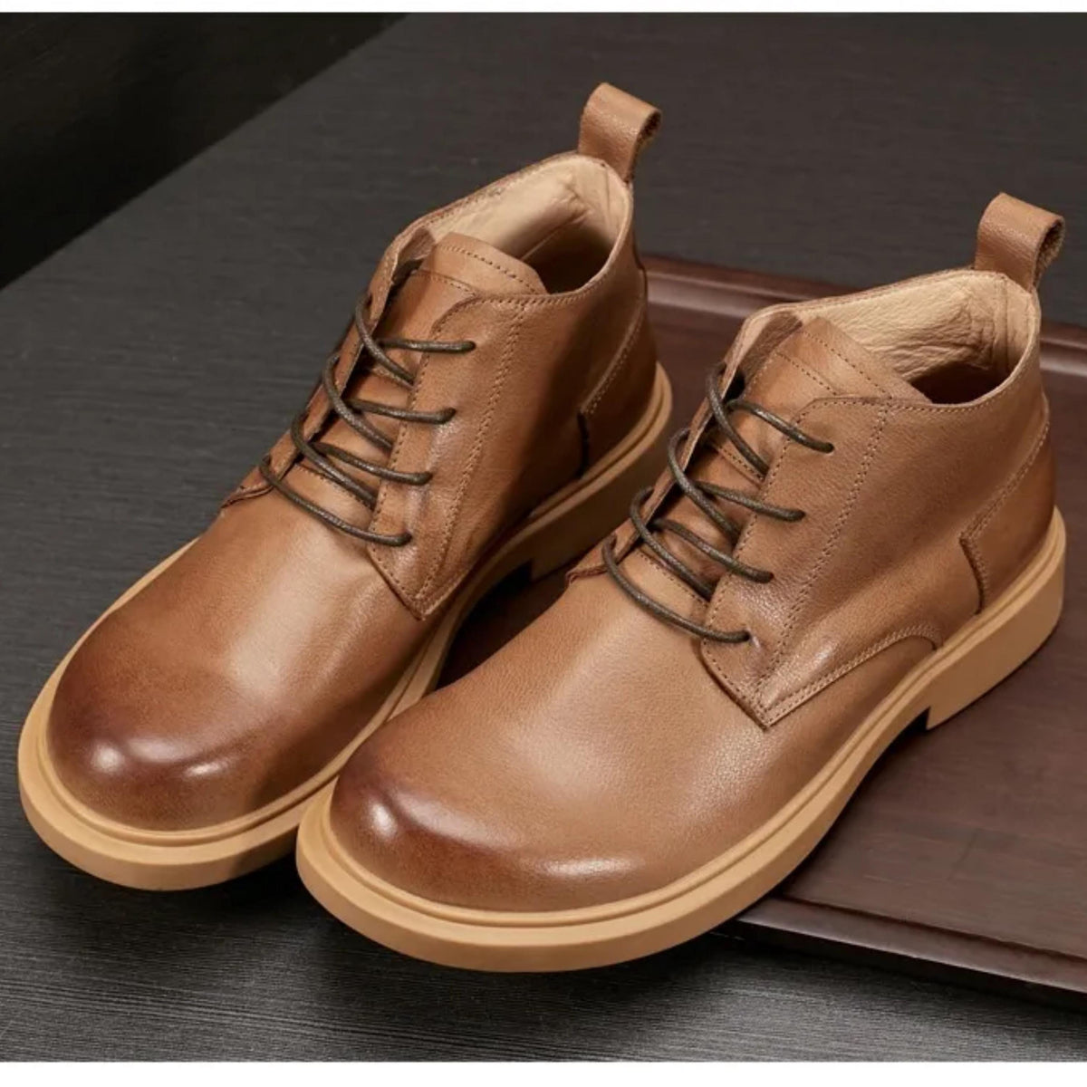 A pair of brown leather boots with laces and a chunky sole, placed on a dark surface.