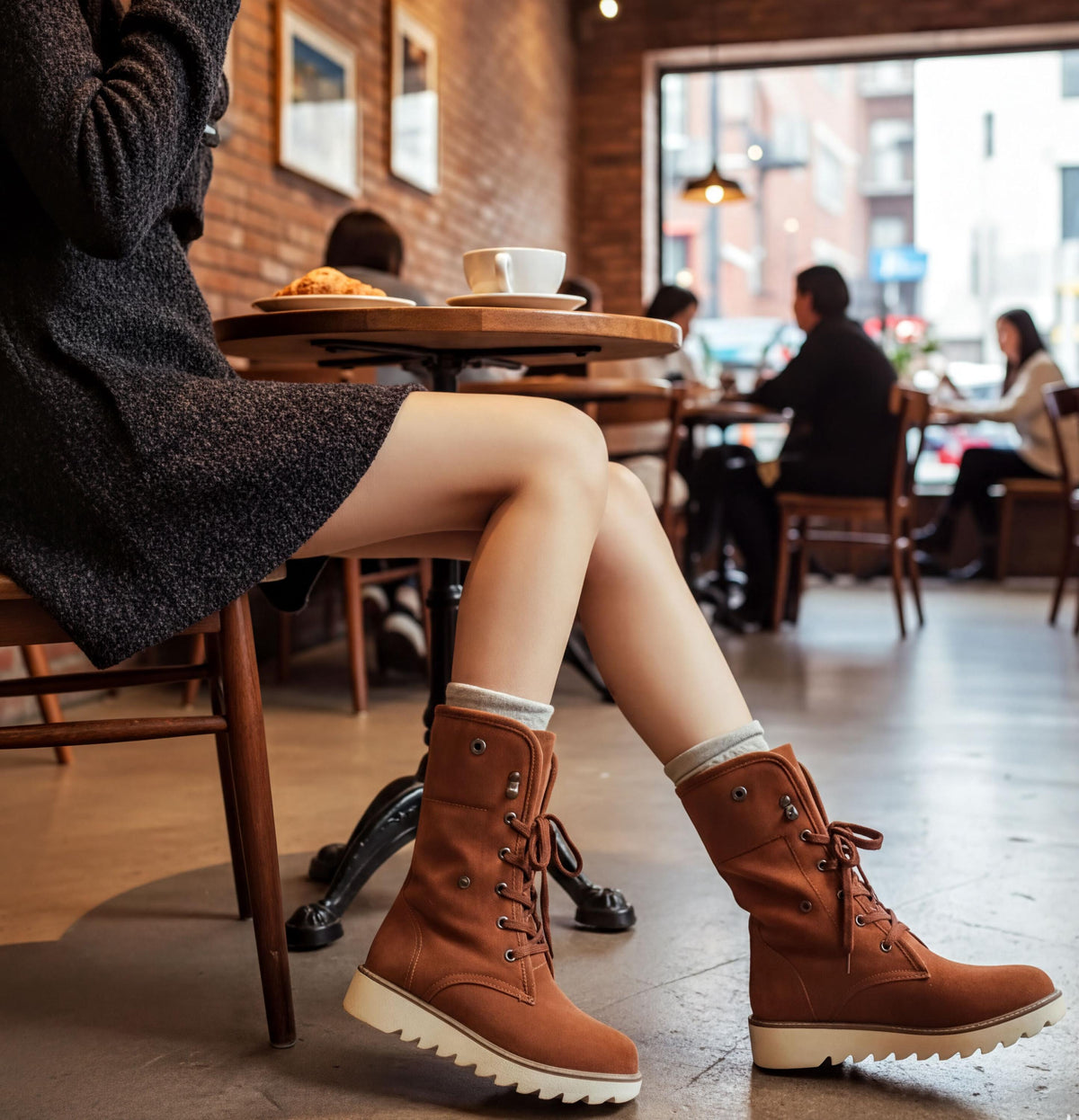 A person is sitting at a table in a cafe, wearing brown boots and a gray sweater.