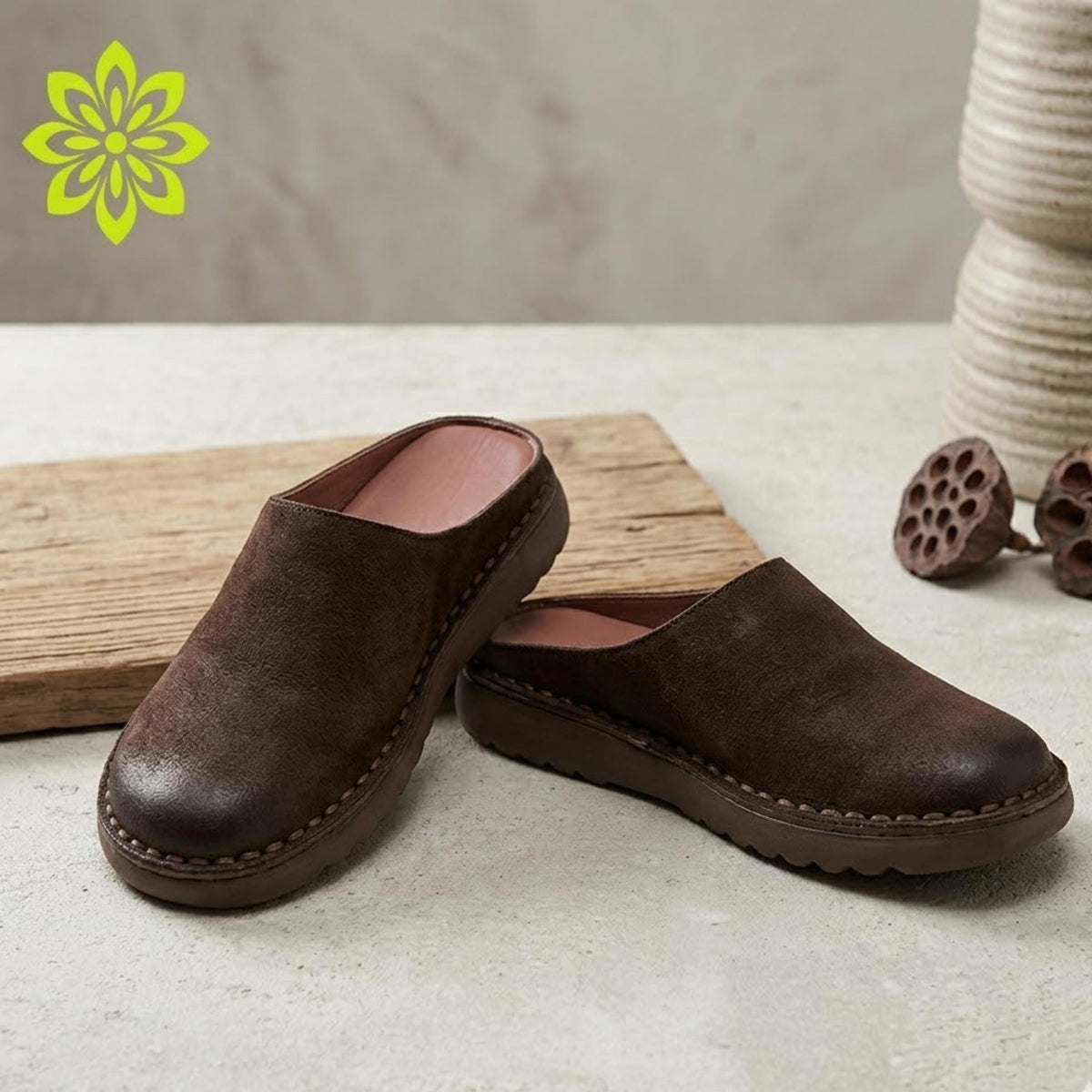A pair of brown suede loafers is placed on a wooden surface, with a green flower-like design in the background.