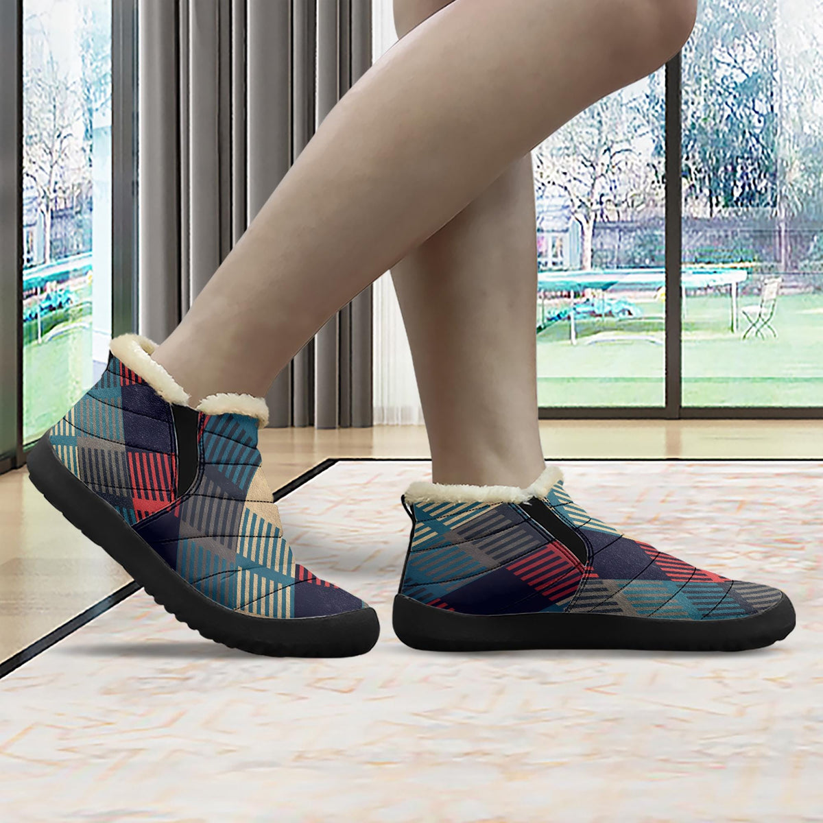 A person's feet wearing colorful patterned boots with fur lining, standing in front of a window with a view of a garden.