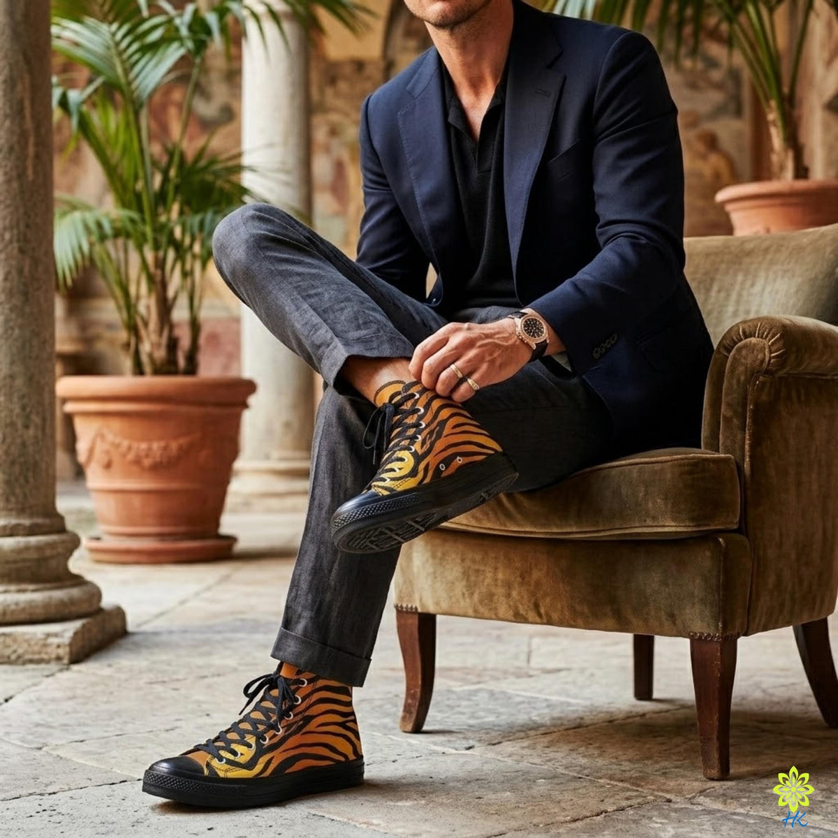 A man wearing a navy blue blazer and black pants sits on a brown armchair, with his feet propped up on a pair of tiger-striped sneakers.