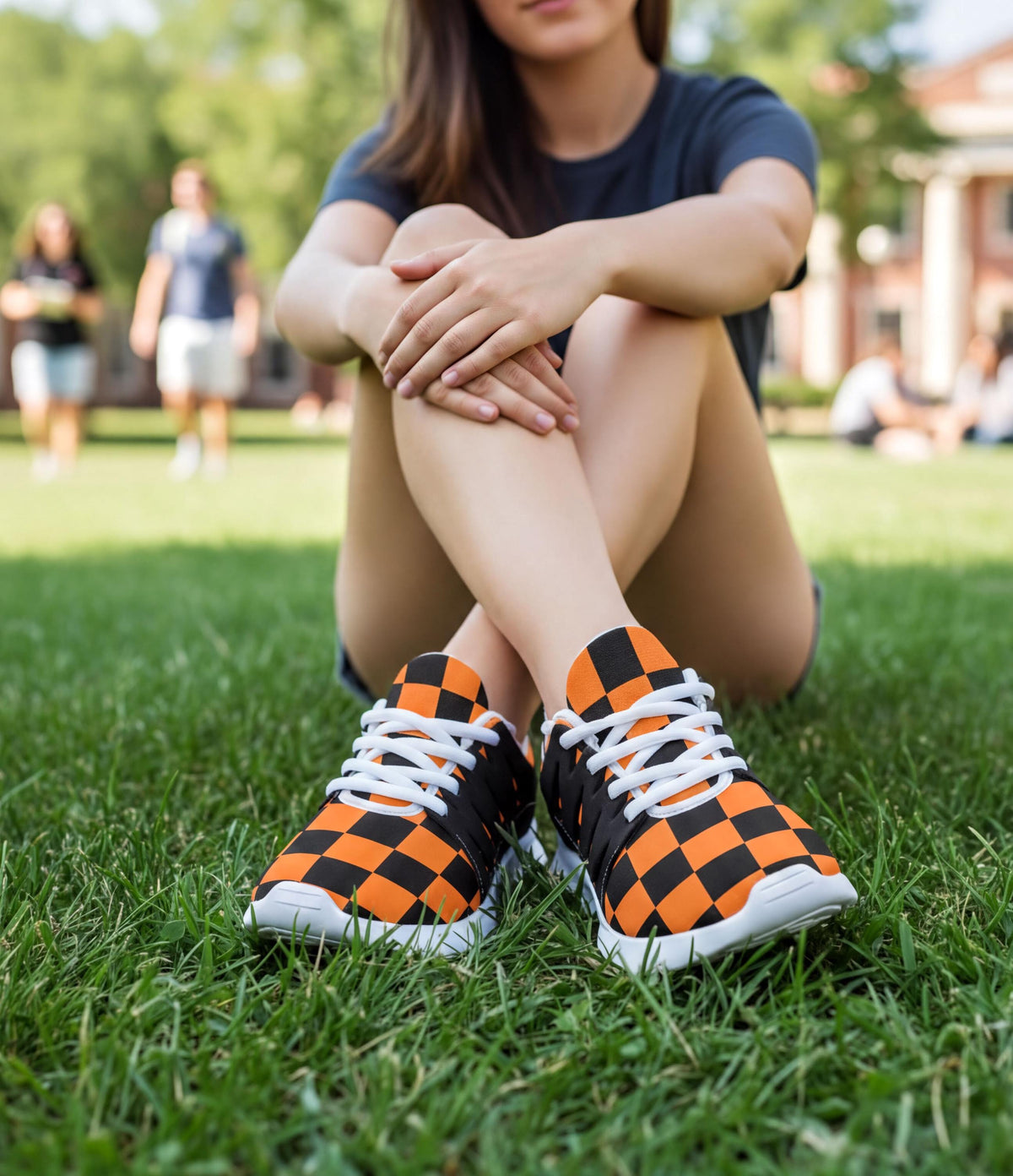 A person sitting on the grass wearing orange and black checkered sneakers.