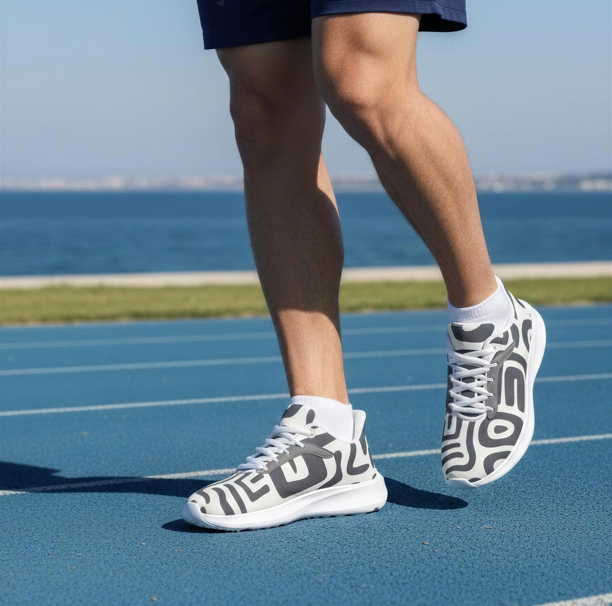 A person wearing patterned sneakers is running on a blue track near the ocean.