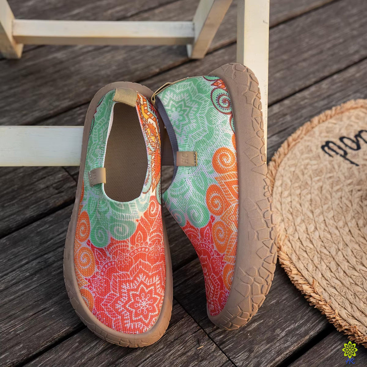 Paio di scarpe slip-on a mandala appoggiate contro uno sgabello bianco su una terrazza in legno