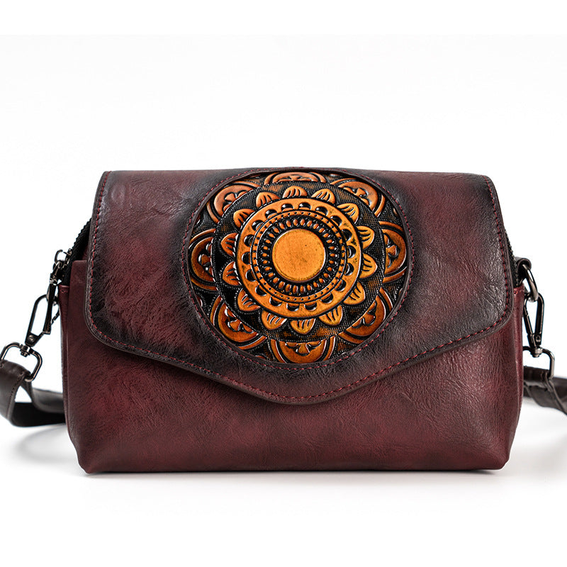 A distressed dark red leather crossbody bag with a large circular floral mandala design in orange and black on the front flap, shown against a plain white background.