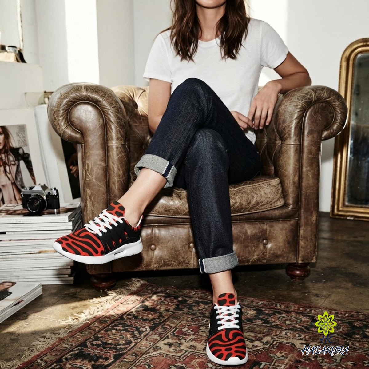 A woman wearing a white t-shirt and jeans is sitting in a brown leather armchair, with her feet propped up on the armrest. She is wearing red and black patterned sneakers.
