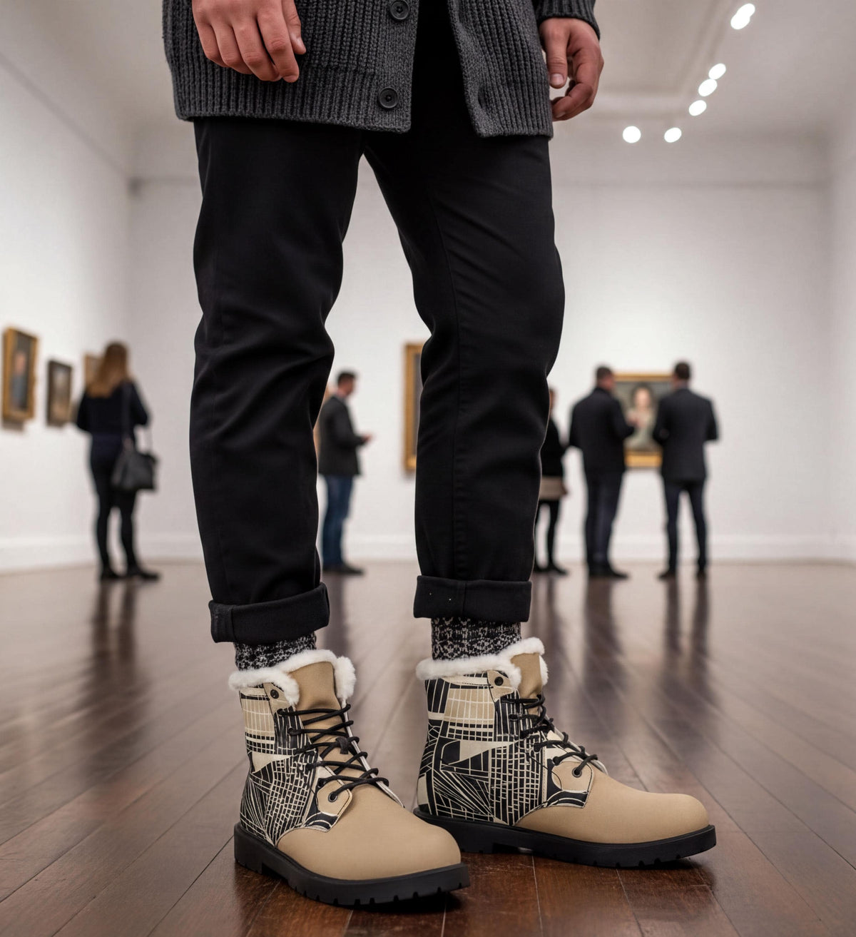 A person wearing black pants and tan boots stands in an art gallery, with other people visible in the background.