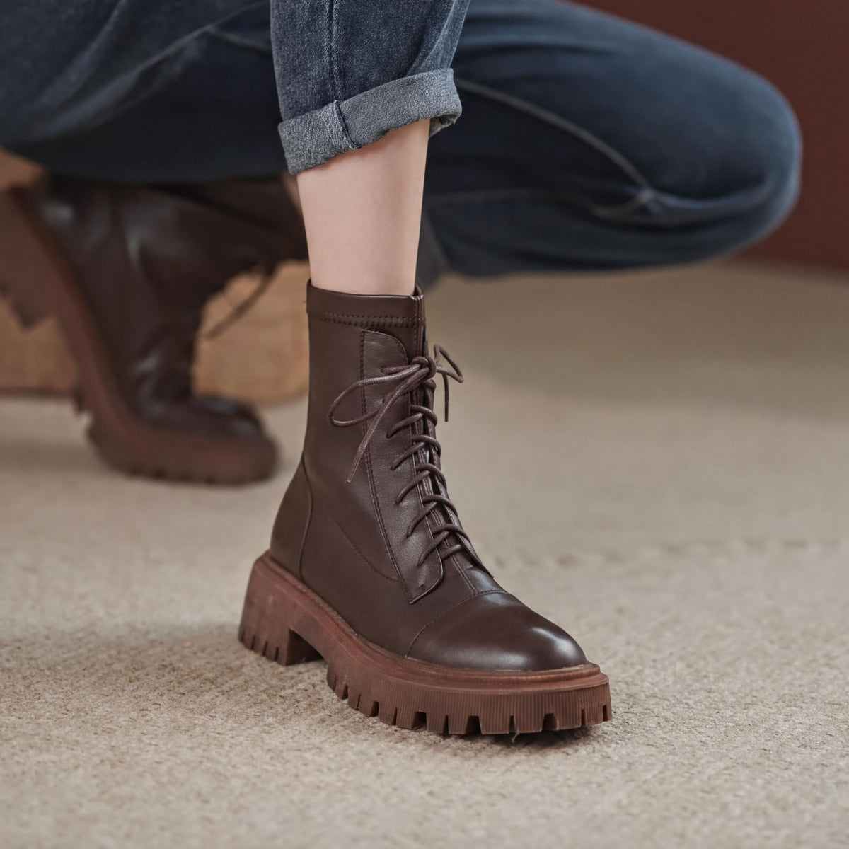 A close-up of a person's foot wearing a brown leather boot with a thick sole and lace-up closure.
