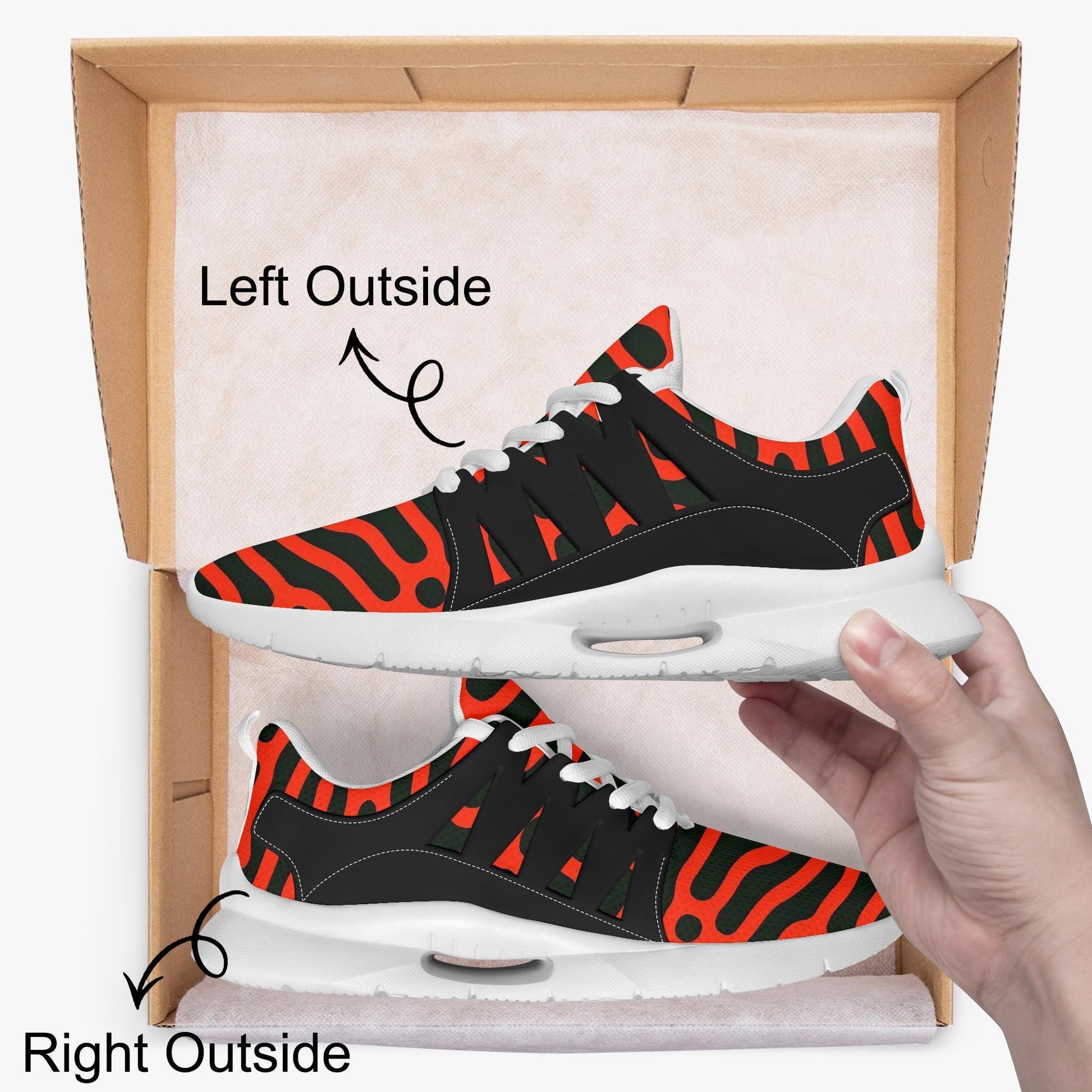 A hand is holding a pair of red and black zebra-striped sneakers, with the left shoe positioned outside the box and the right shoe inside the box.