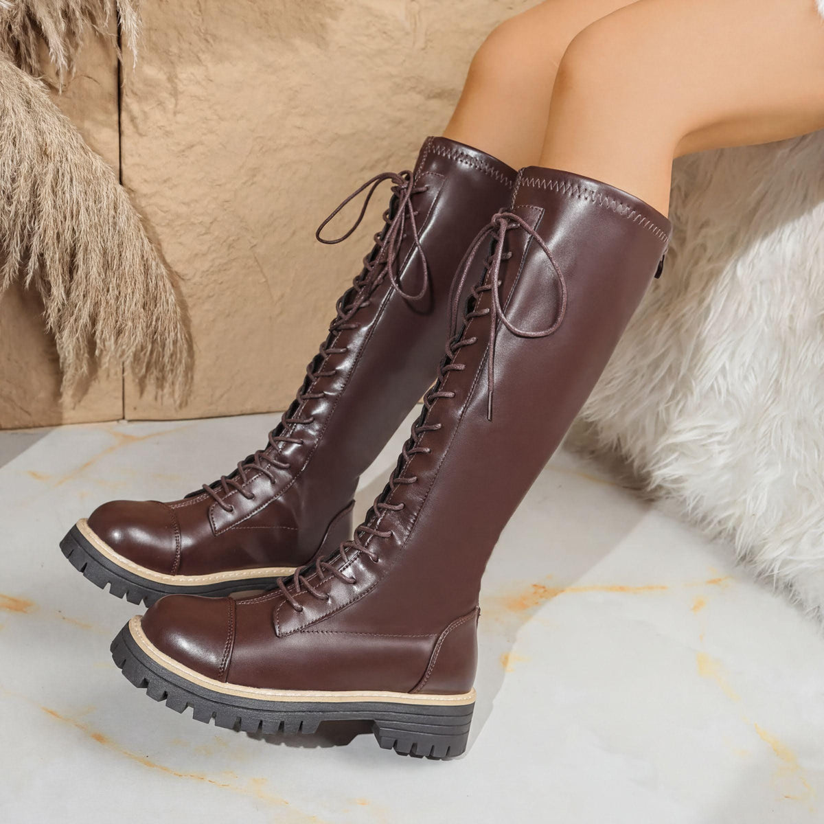A pair of brown leather boots with laces and a chunky sole, placed on a white surface.
