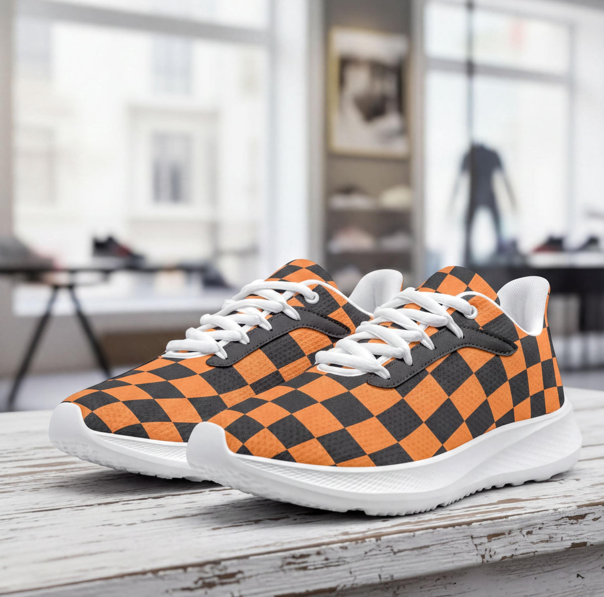 A pair of orange and black checkered sneakers is displayed on a wooden surface, with a blurred background that includes a window and a person.