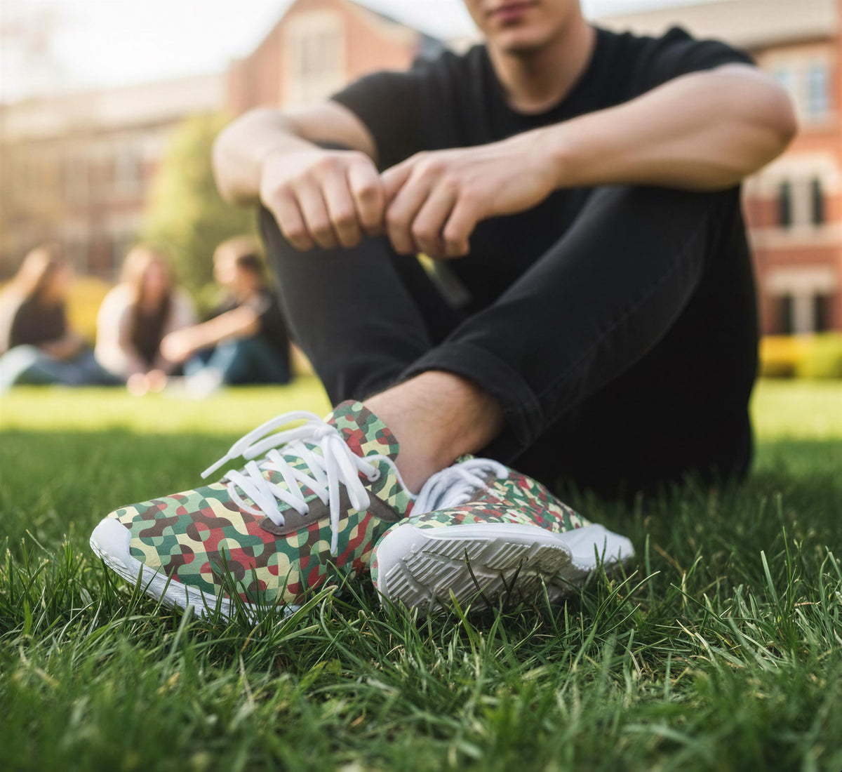 A person sitting on the grass wearing camouflage sneakers.