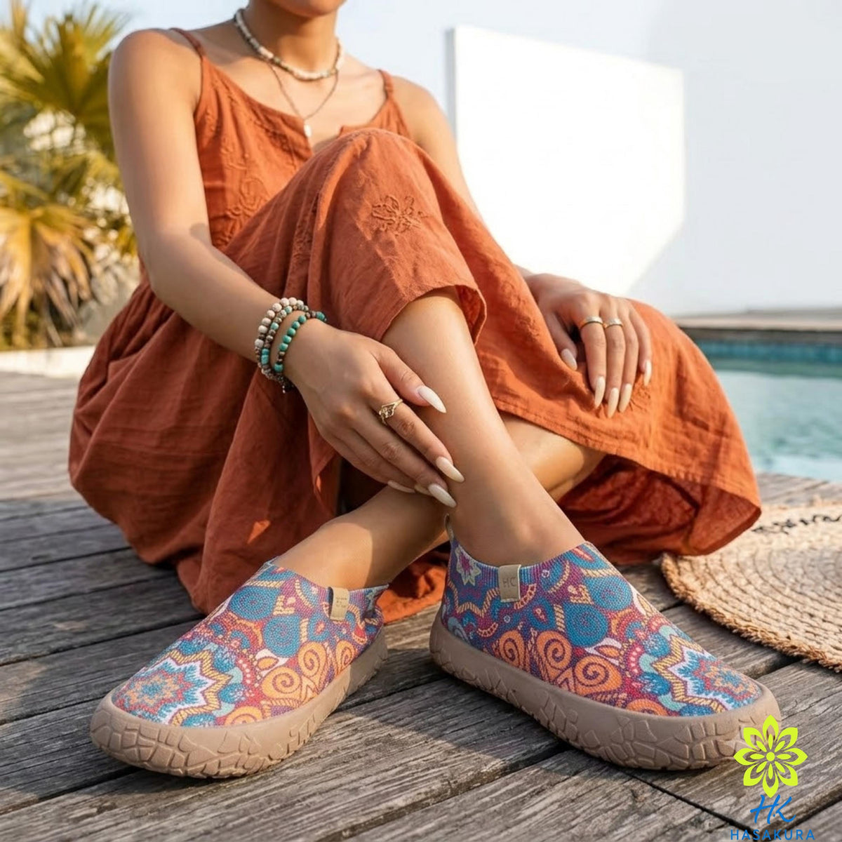 A woman in an orange dress sits on a wooden deck, wearing colorful patterned shoes and accessorized with bracelets and rings.