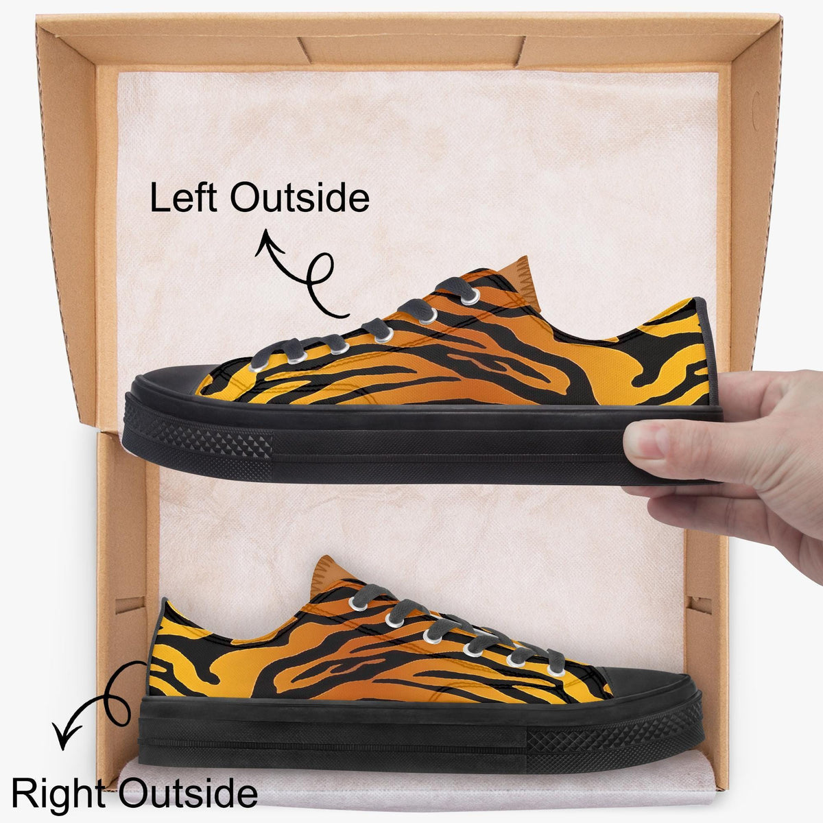 A hand is holding a pair of tiger-striped sneakers, with the left shoe positioned inside the box and the right shoe outside the box.