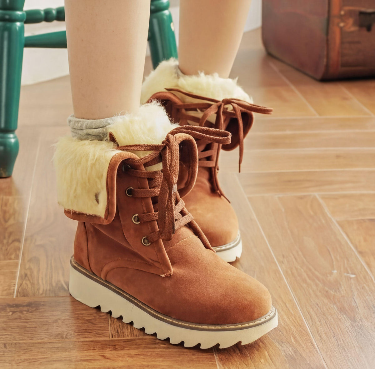 A pair of brown boots with white fur lining, standing on a wooden floor.
