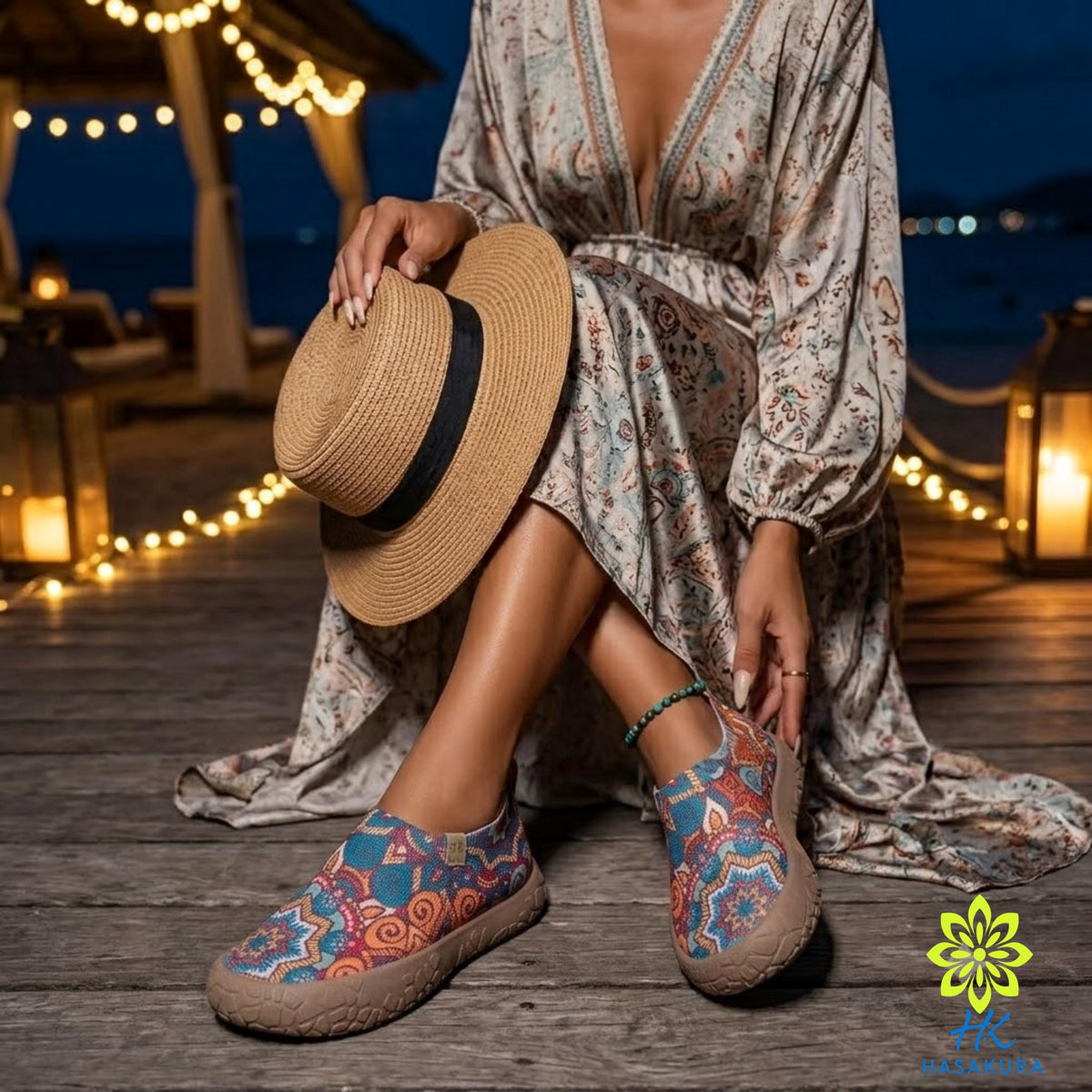 A woman in a patterned dress and colorful shoes sits on a wooden deck at night, holding a straw hat and wearing a bracelet.