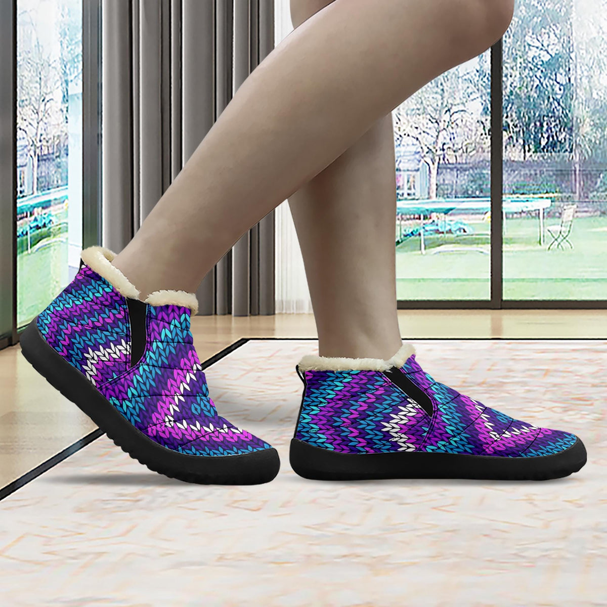 A person's feet wearing colorful, patterned, and textured shoes, standing in front of a window with a view of trees outside.