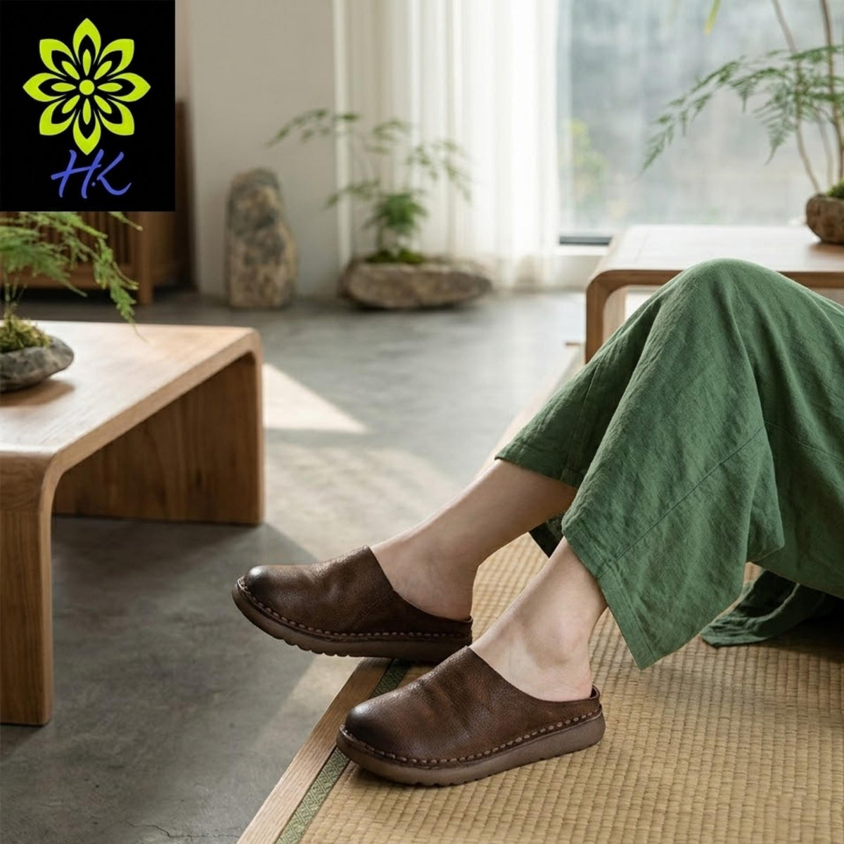 A person's legs wearing brown slip-on shoes are shown in a living room setting with potted plants and a wooden coffee table.