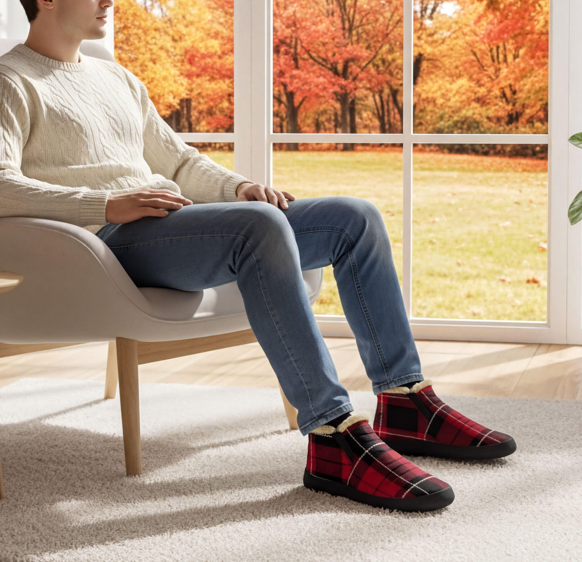 A person is sitting in a chair, wearing a white sweater and blue jeans, with red and black plaid shoes, and looking out a window at a colorful autumn landscape.
