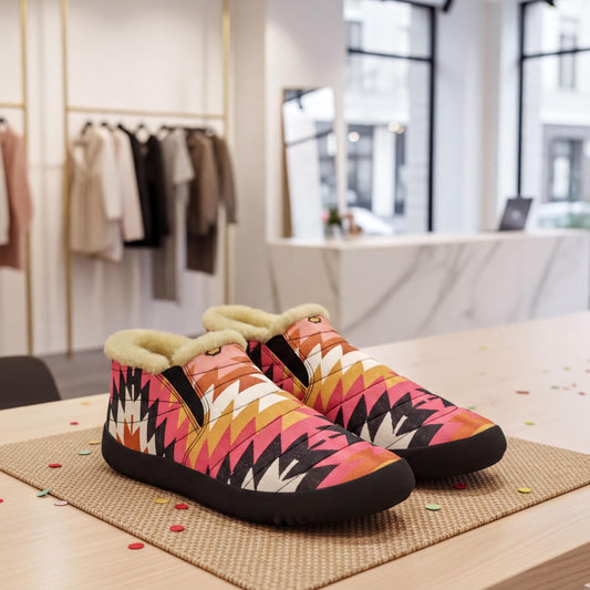 A pair of colorful, patterned shoes is displayed on a table in a clothing store, with clothing racks and a counter visible in the background.
