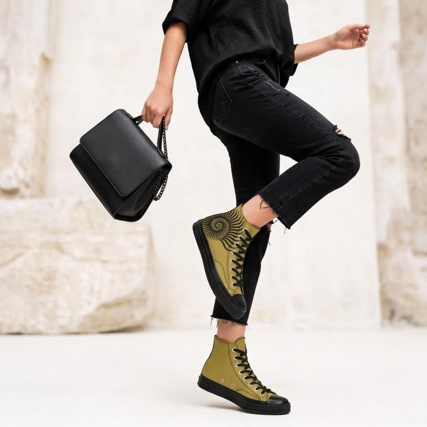 A person wearing black pants and yellow sneakers is standing on one leg, holding a black handbag in their other hand.