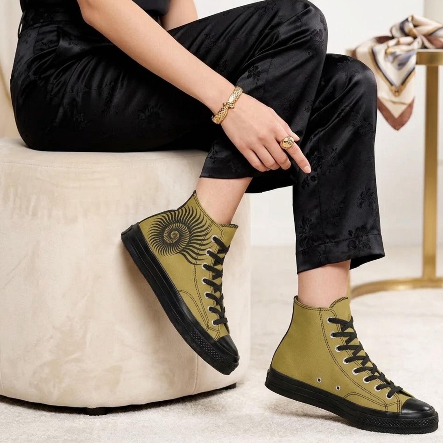 A person sitting on a white stool wearing black pants and yellow high-top sneakers with a sun design on the side.