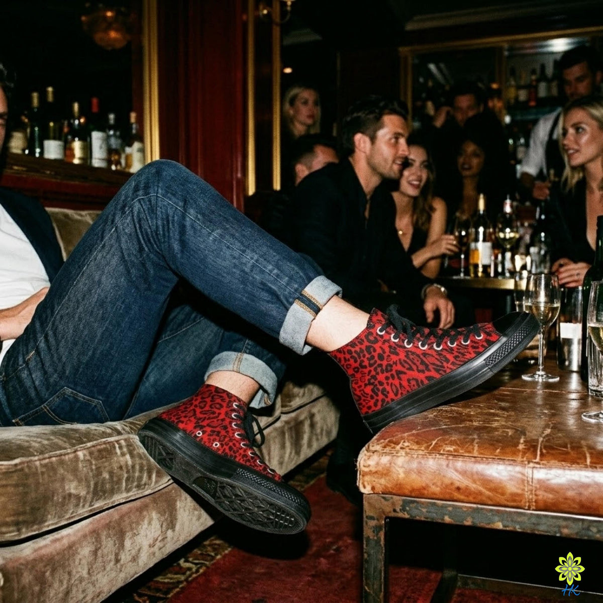 A person wearing red and black sneakers is sitting on a couch in a bar, surrounded by other people and wine glasses.