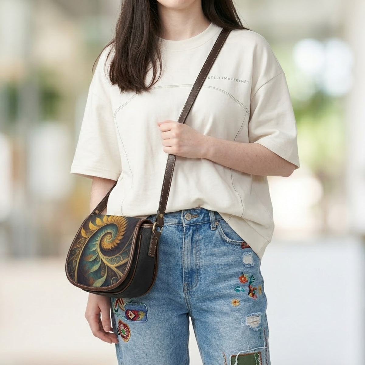 Model draagt schuin over het lichaam gedragen saddle bag schoudertas met crèmekleurige trui en jeans