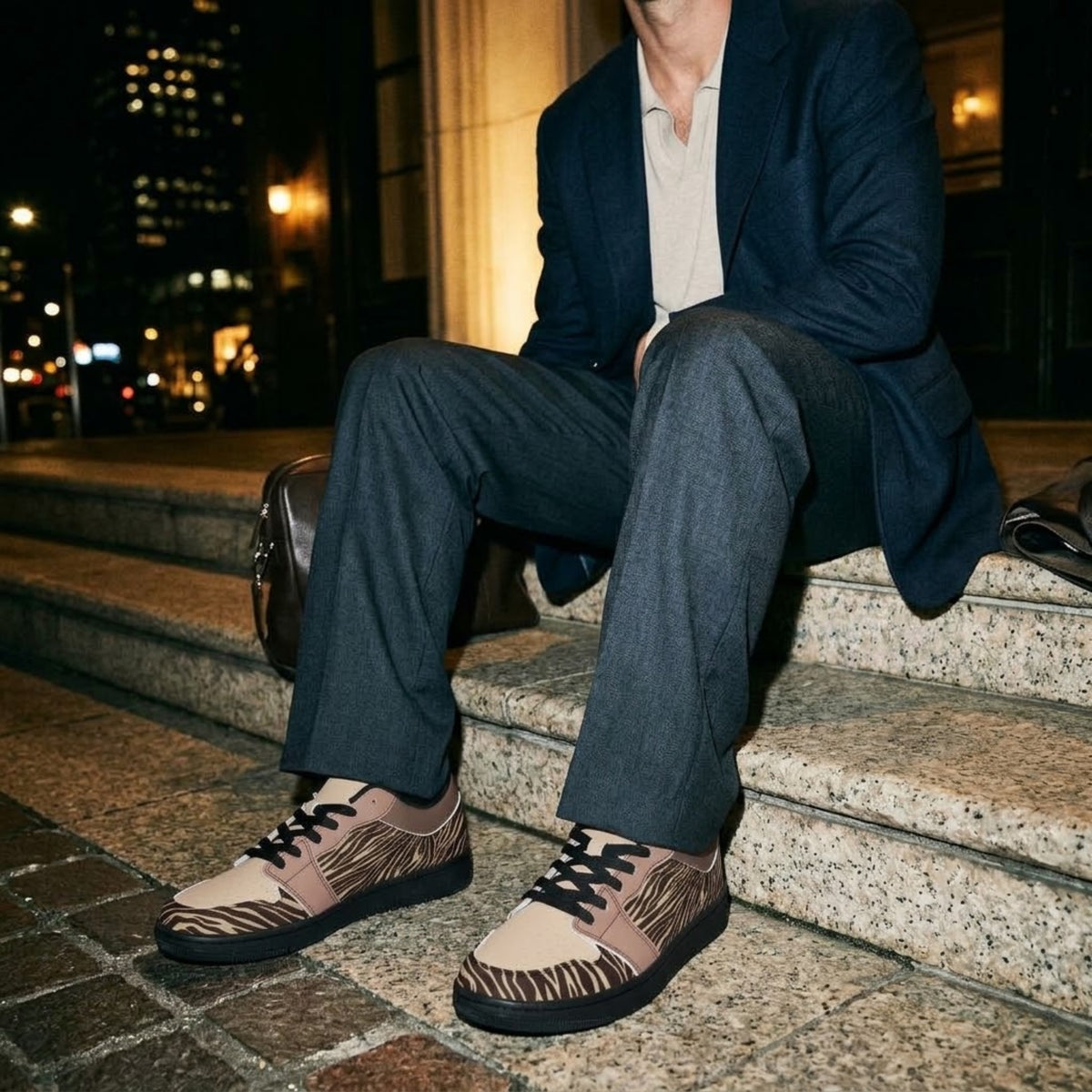 Model seated at night in dark trousers and blazer wearing sneakers