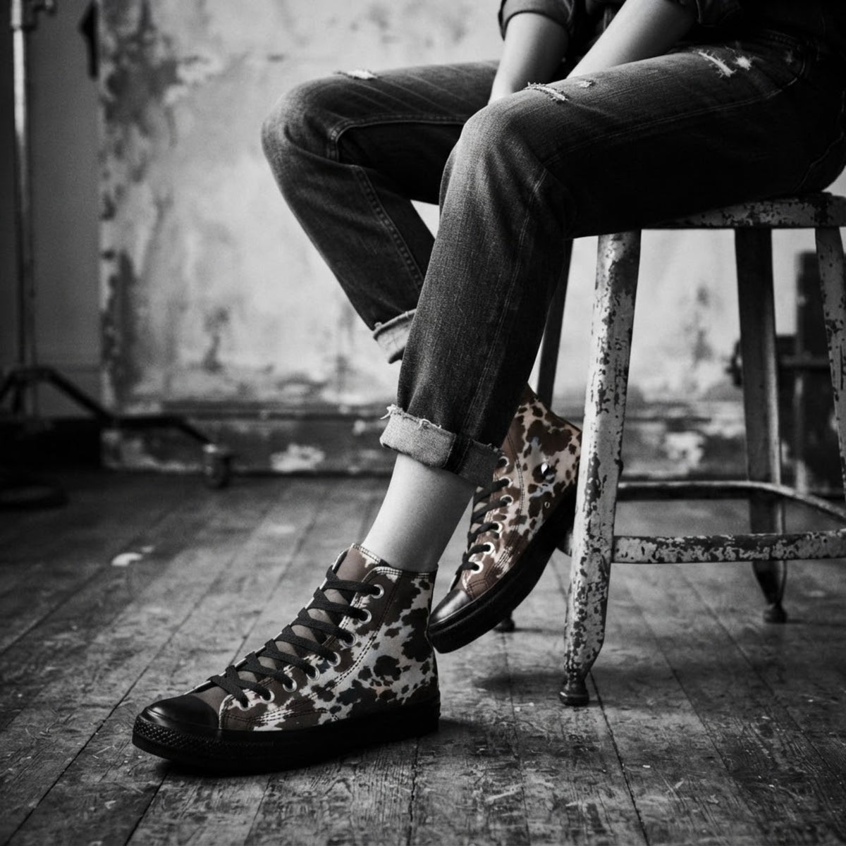 Sneakers alte a stampa mucca indossate con jeans scuri risvoltati su uno sgabello e una cassa