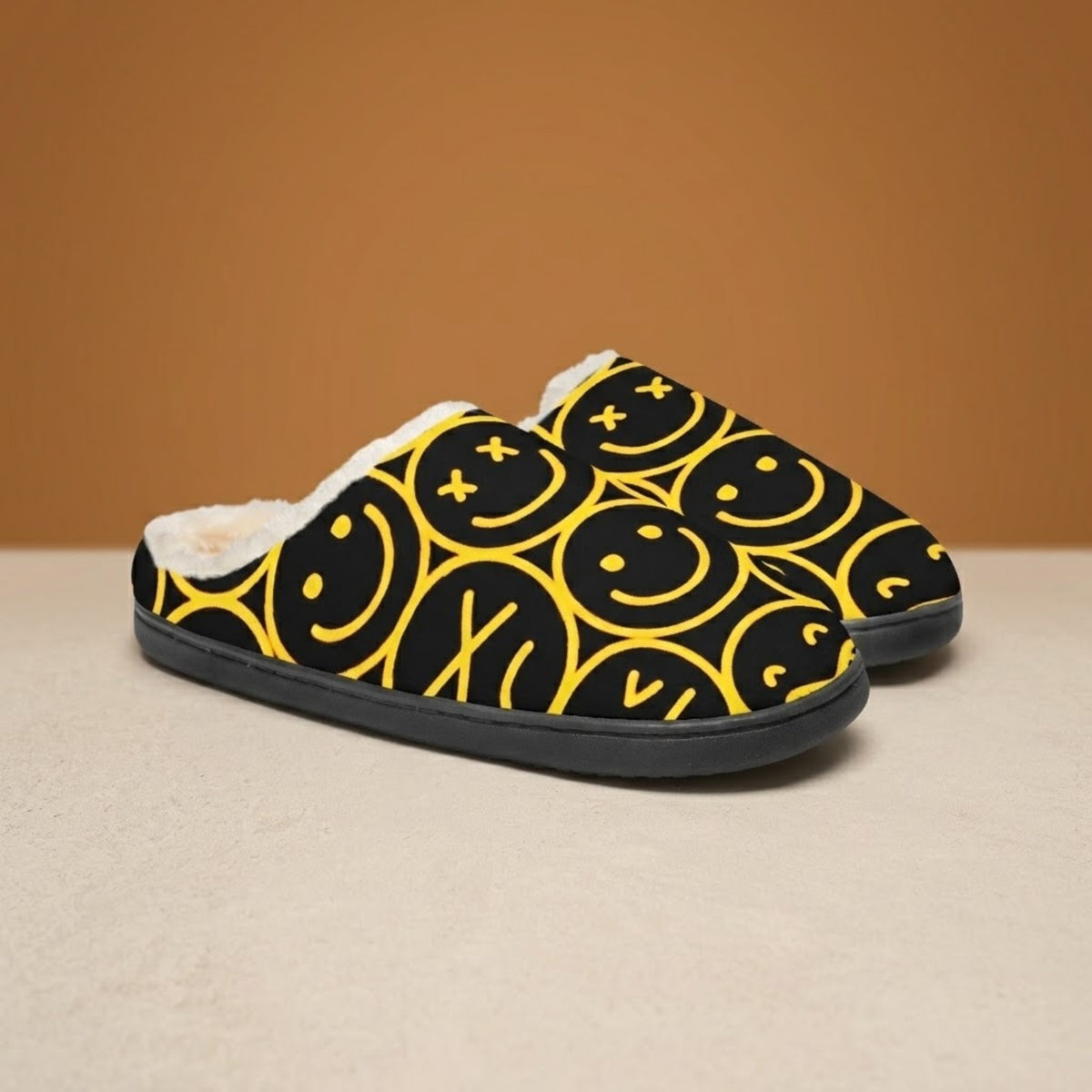 Smiley face slippers in black with yellow smiley pattern, front three-quarter view on beige background