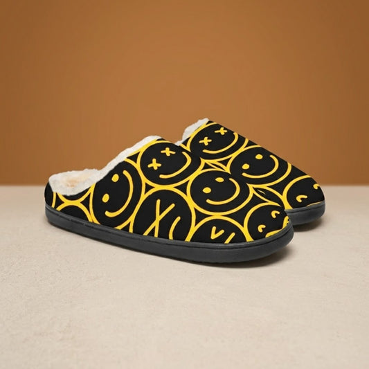 Smiley face slippers in black with yellow smiley pattern, front three-quarter view on beige background