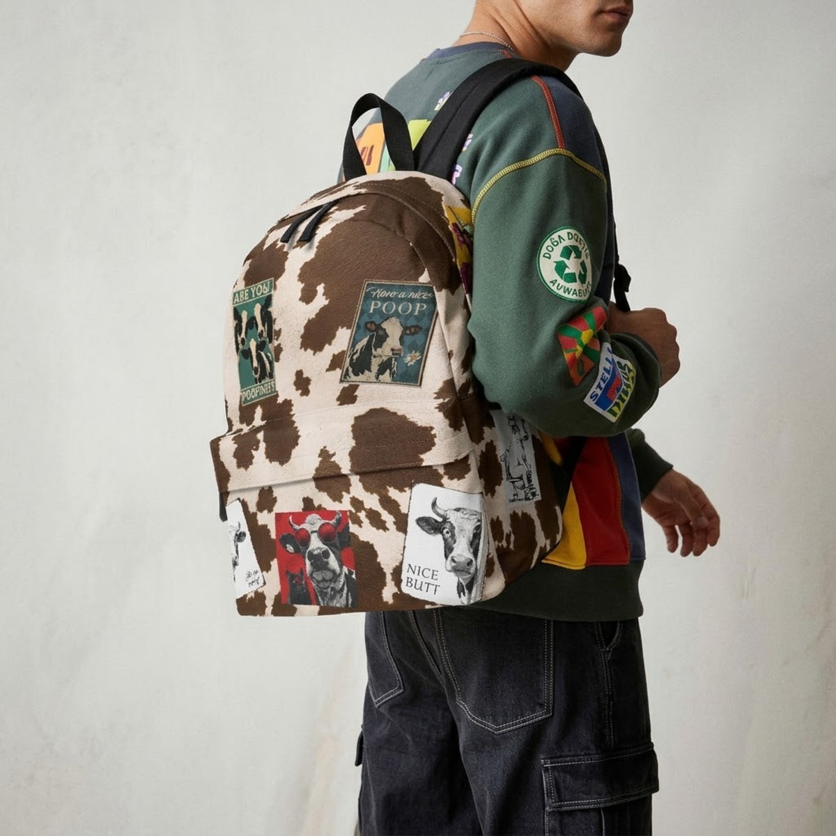 Hombre con una mochila de vaca con parches frente a una pared clara
