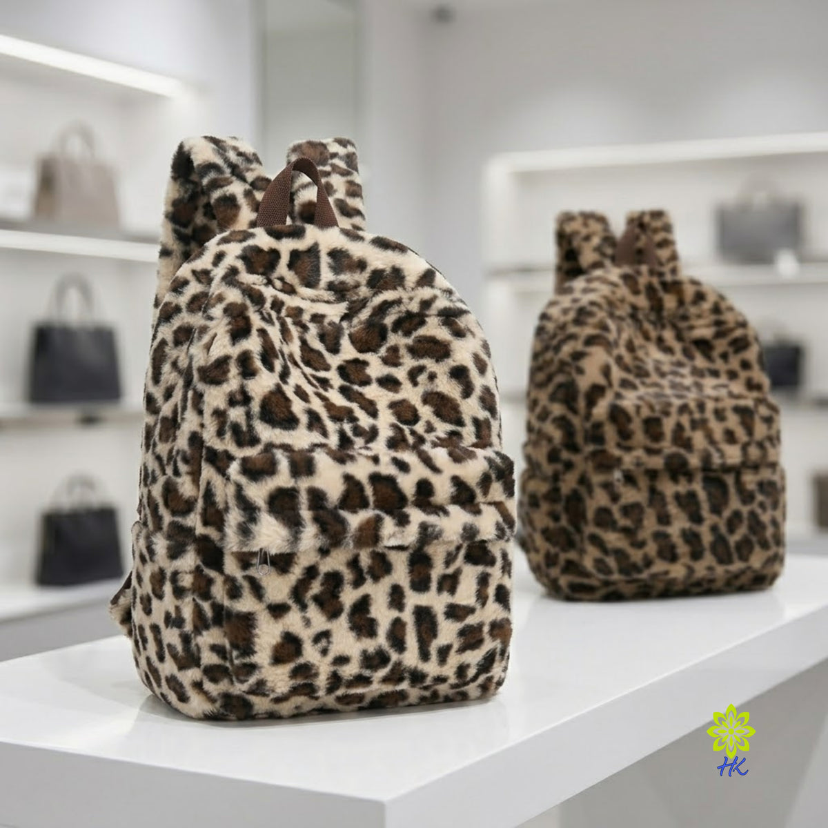 Two leopard-print faux fur backpacks displayed on a white shelf in a boutique setting. The foreground backpack is beige with black and brown spots, and the background backpack is a darker brown and tan pattern.